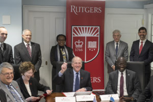 People sitting at and standing around a conference room table, with a Rutgers banner in the background.