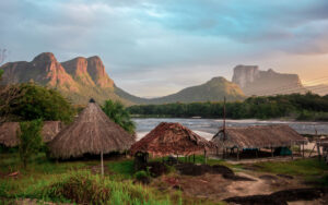 an indigenous camp with a river and mountains in the background