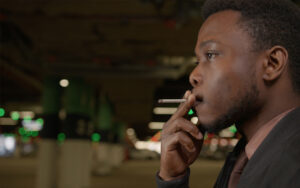 A Black person leaning against a building, smoking